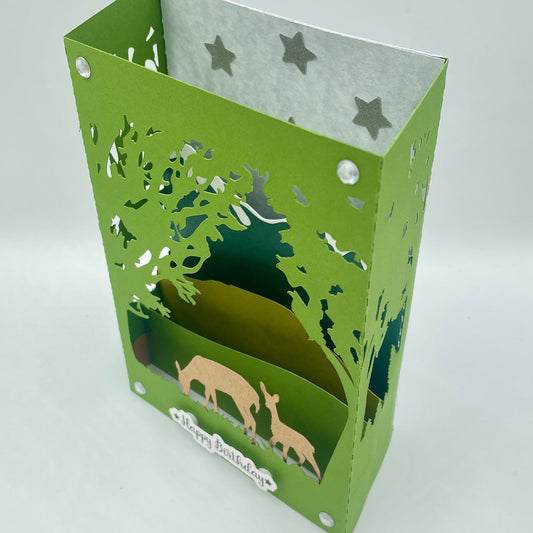 Green paper lantern with cut-out designs of trees and animals on a white background