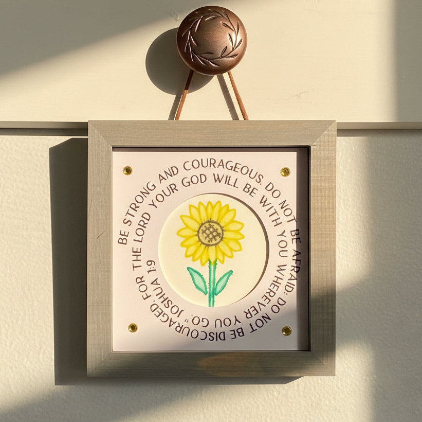 Decorative wall art with a sunflower illustration and motivational text on a light background.