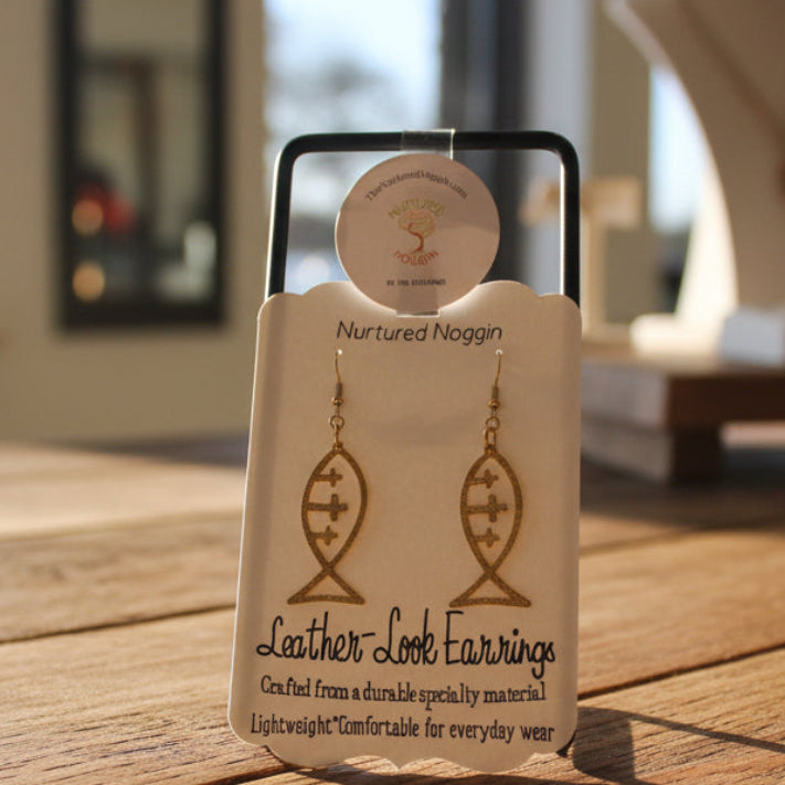 Pair of gold fish-shaped earrings on a branded card with a blurred jewelry store background.