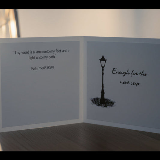 Greeting card with lamp illustration and text next to a lantern on a wooden surface.