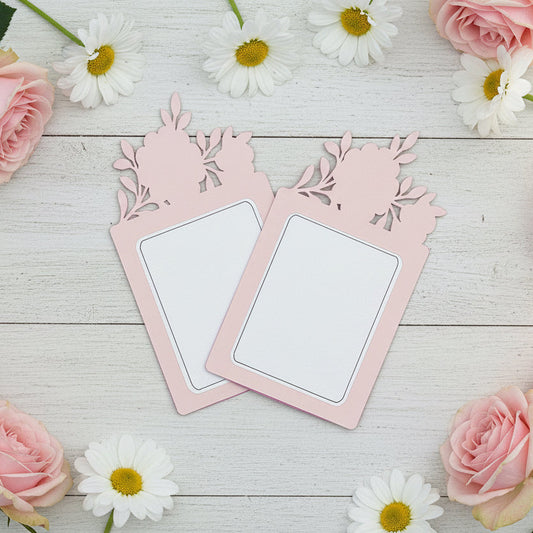 Two pink floral cards on a wooden surface with pink roses and white daisies.