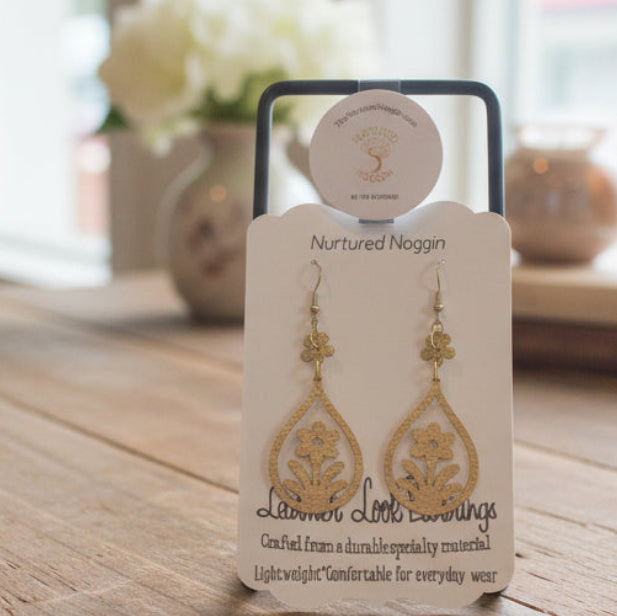 Gold earrings on a branded card on a wooden surface with a blurred background