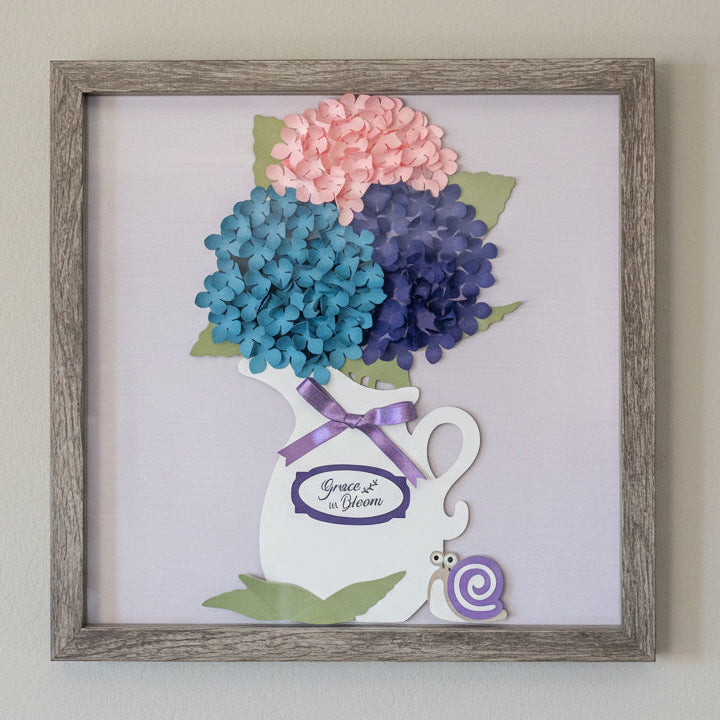 Shadowbox with paper flowers in a pitcher on a light background