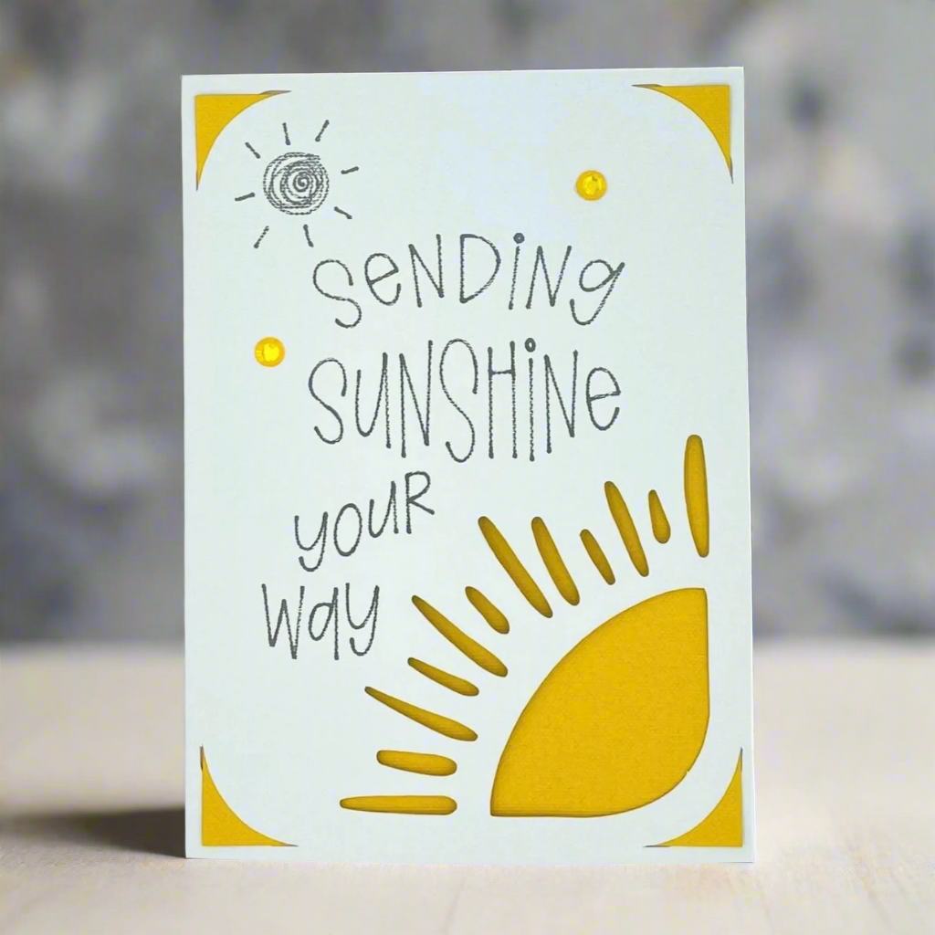 A greeting card with a yellow sun design and the text 'SENDING SUNSHINE YOUR WAY' along with a few dots to represent sun rays.