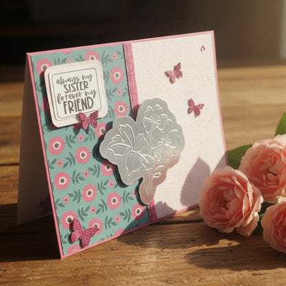 Greeting card with floral design and text, placed on a wooden surface with pink flowers.