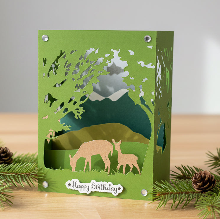 Green birthday card with cut-out design of deer in a forest, featuring 'Happy Birthday' text.