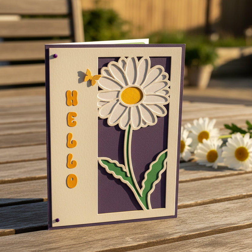 Greeting card with a daisy design and 'hello' text on a wooden surface outdoors.
