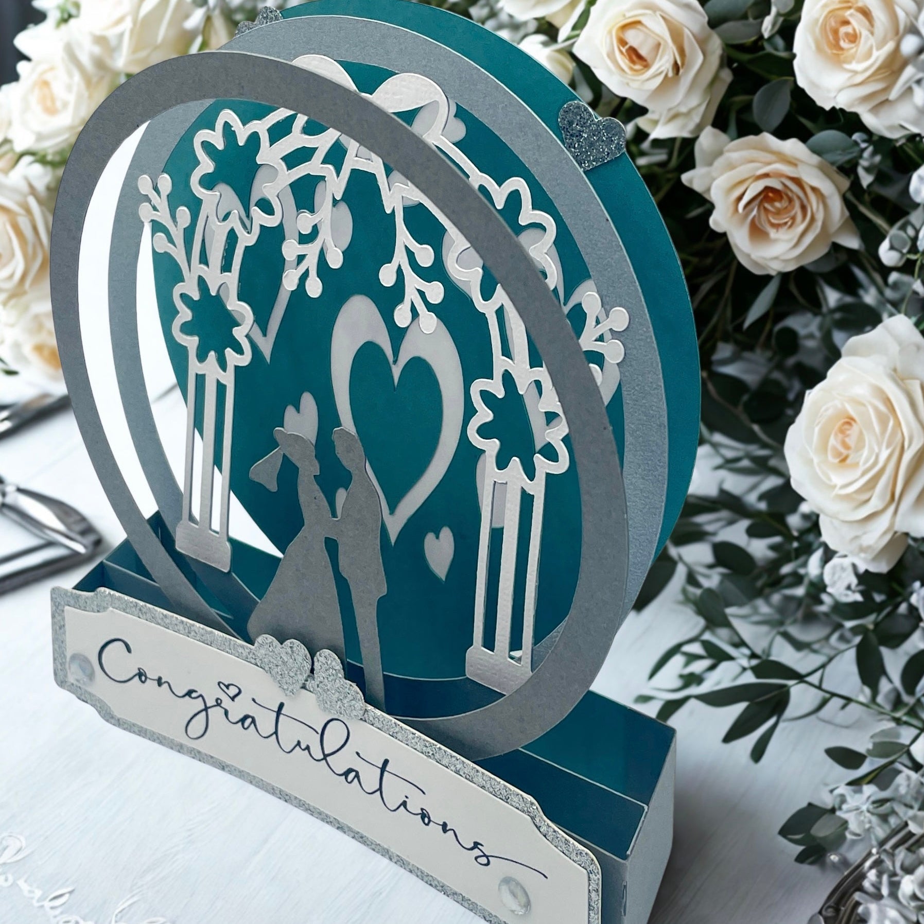 Decorative wedding card with cut-out design of a couple under an arch, surrounded by white roses.