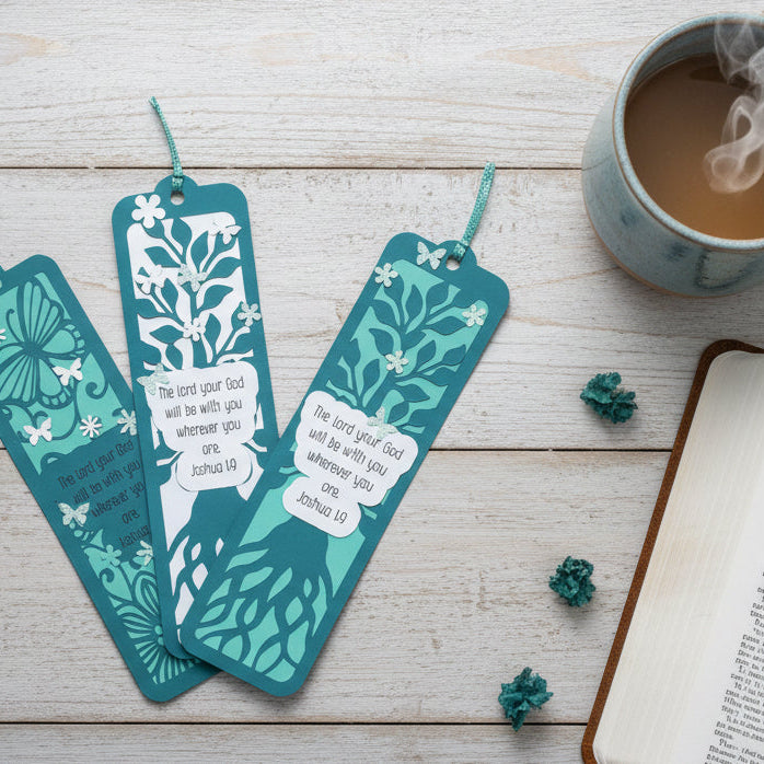 Teal bookmarks with floral designs on a wooden surface with an open book and mug of coffee.