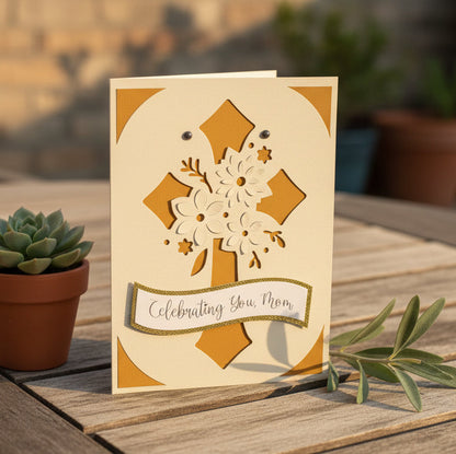 Greeting card with floral design and 'Celebrating You Mom' text on a wooden surface with a potted plant.