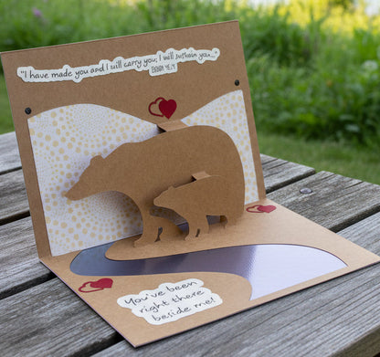 Card with bear cutout and text on a wooden surface outdoors
