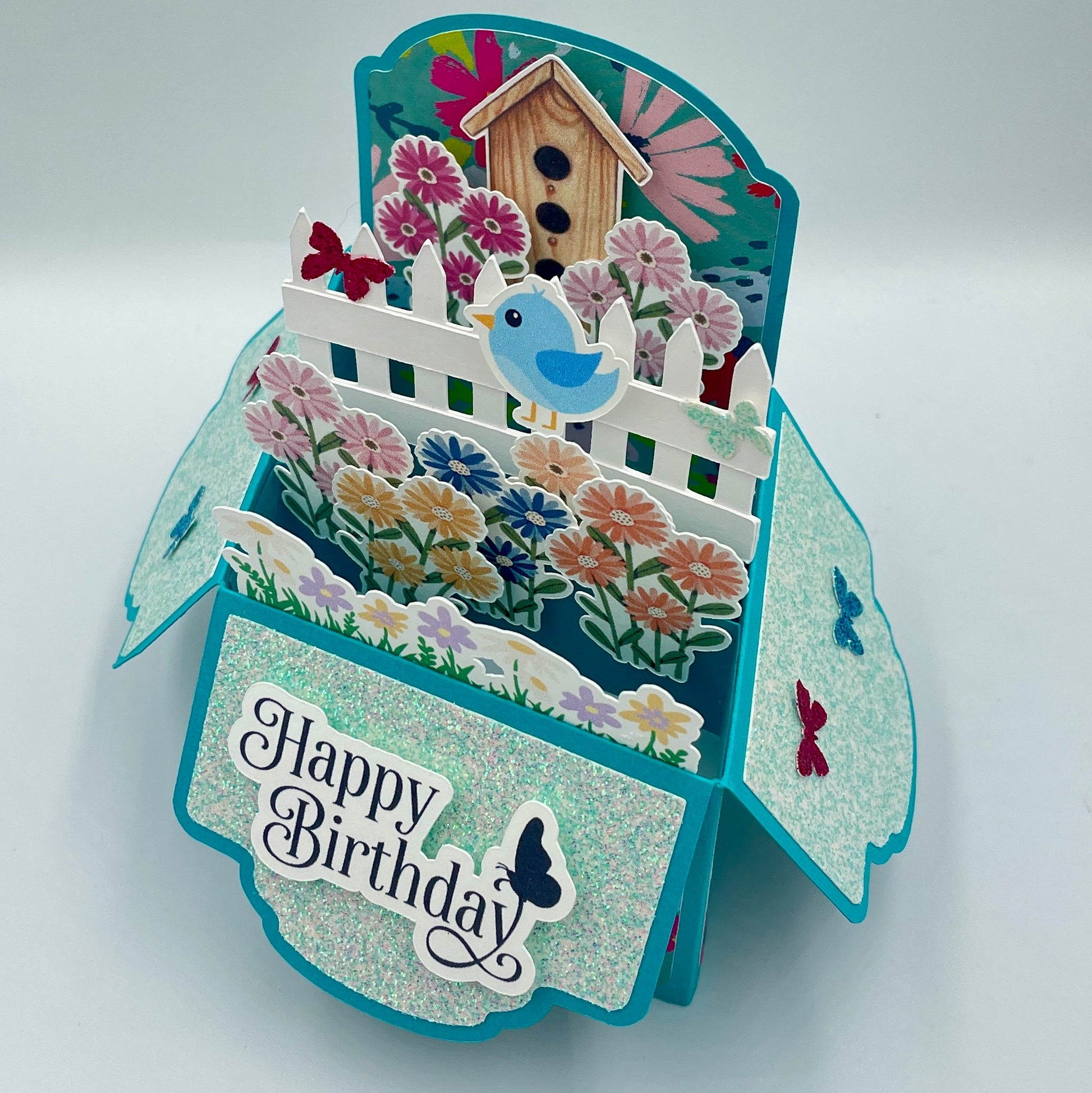 Decorative birthday card with flowers, birdhouse, and 'Happy Birthday' text on a white background