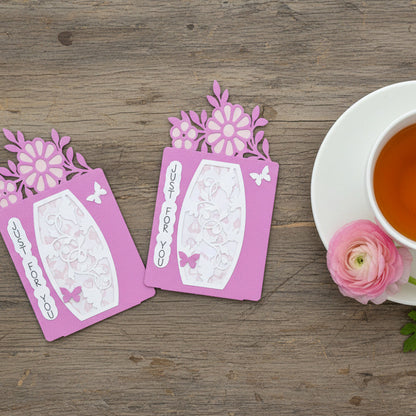 Two pink floral cards on a wooden surface with a cup of tea and a flower.