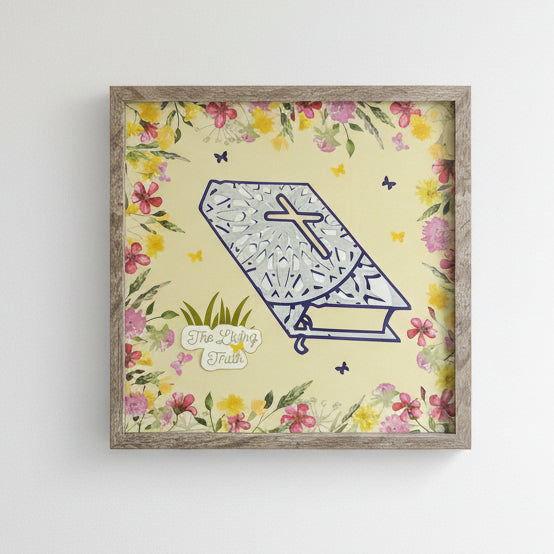 Decorative shadowbox with a cross design and floral border on a yellow background, featuring 'The Living Truth' logo.