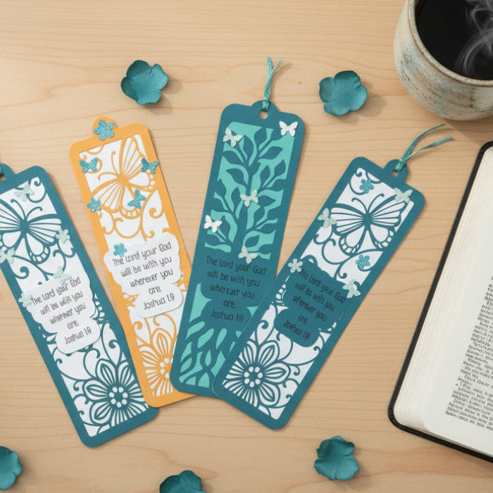 Decorative bookmarks with floral and butterfly designs on a wooden surface with an open book and coffee mug.