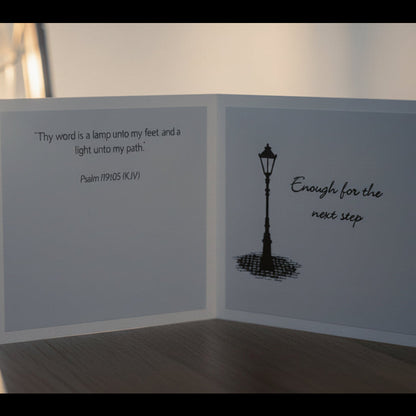 Greeting card with lamp illustration and text next to a lantern on a wooden surface.