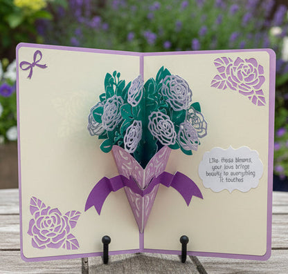 Pop-up card with floral design and message on a wooden surface with blurred flowers in the background