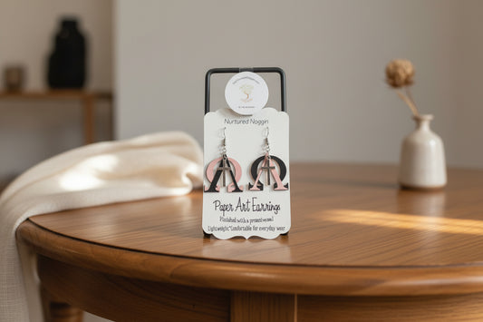 Pair of paper art earrings on a branded card against a gray background