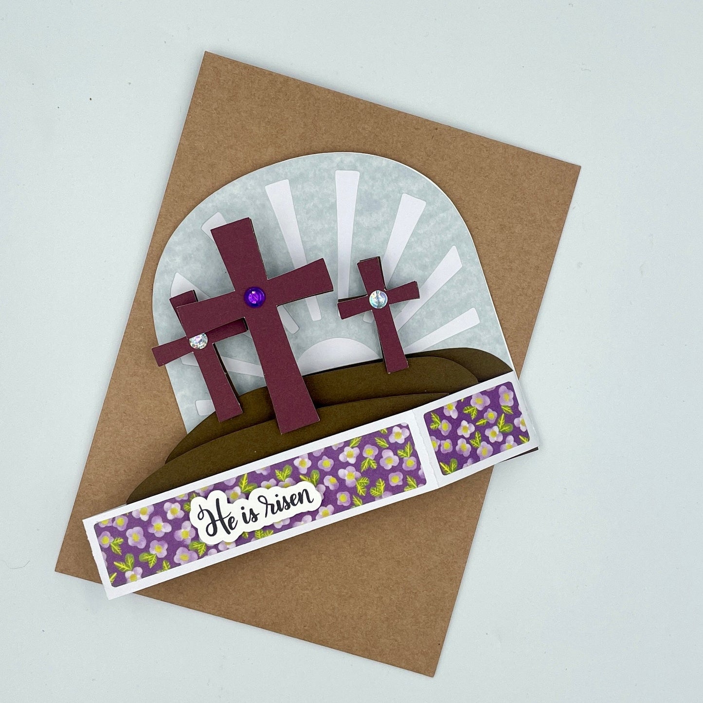 Easter-themed card with crosses and 'He is risen' text on a brown envelope.