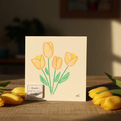 Card with yellow tulips illustration and text, surrounded by real yellow tulips on a wooden surface.